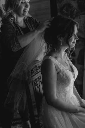Black and white image of wedding preparations with bride getting her veil adjusted.