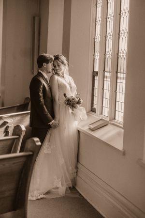 Romantic sepia-toned portrait of newlyweds by church window.