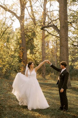 A couple dances in a wooded area during golden hour, with the bride's dress flowing gracefully.