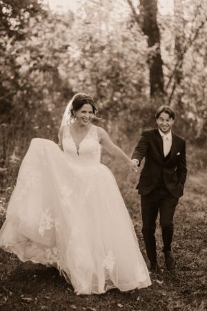 A joyful moment captured in sepia tones as a couple walks through an autumn woodland setting.