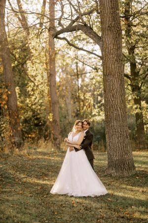 A romantic embrace in a sun-dappled forest with golden light filtering through the trees.
