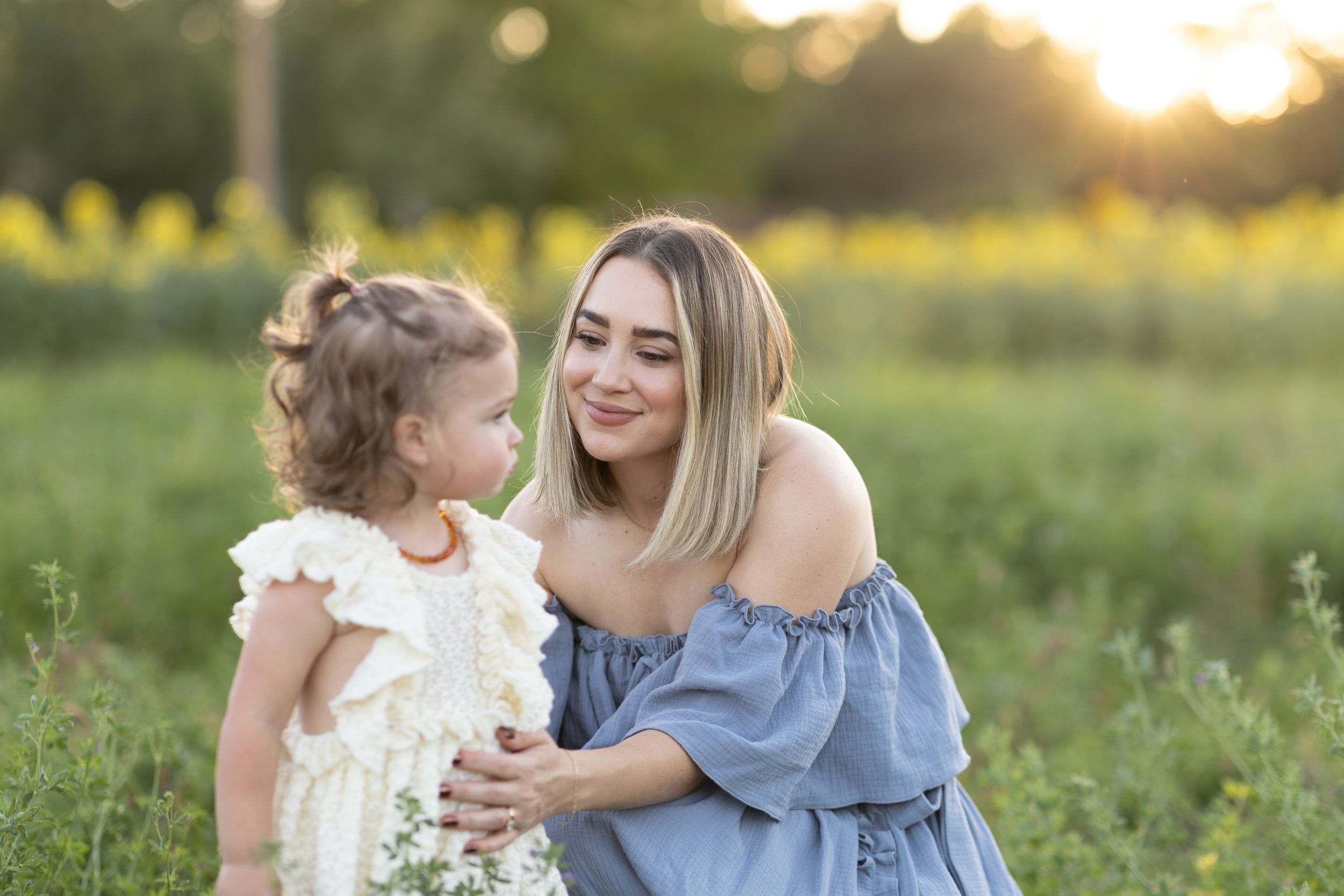 A touching moment between two people in a field at golden hour with soft sunlight and greenery in the background.