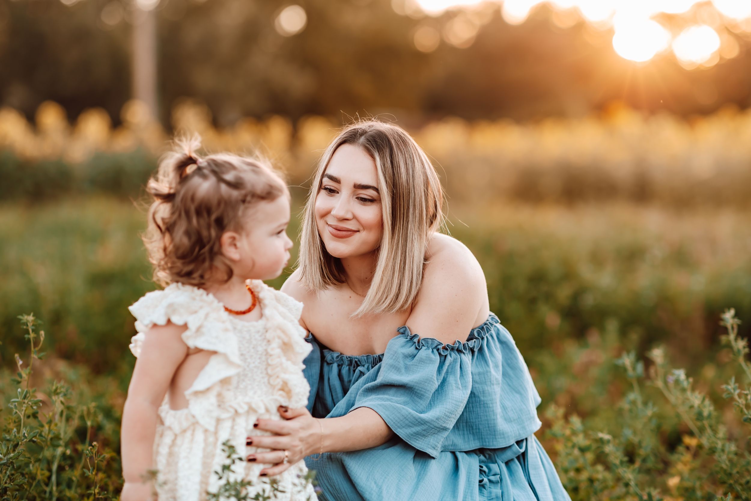 Two people share a tender moment in a meadow at sunset with golden light filtering through trees in the background.