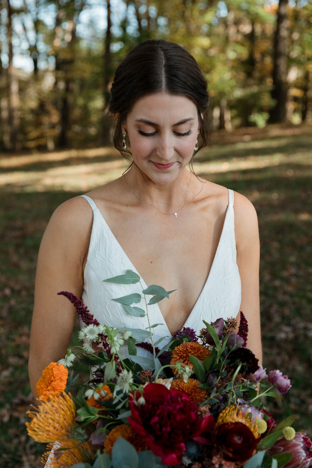 A fall wedding bouquet with deep burgundy and orange flowers against a white dress.