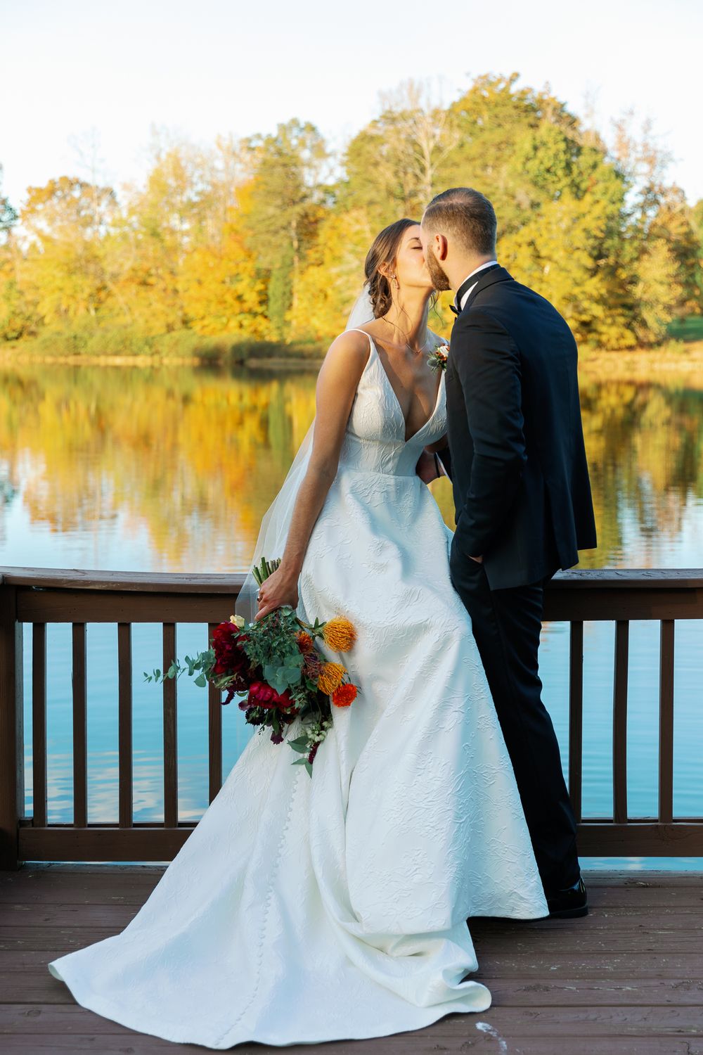 A couple shares a romantic moment on a wooden deck overlooking a serene lake during golden hour.