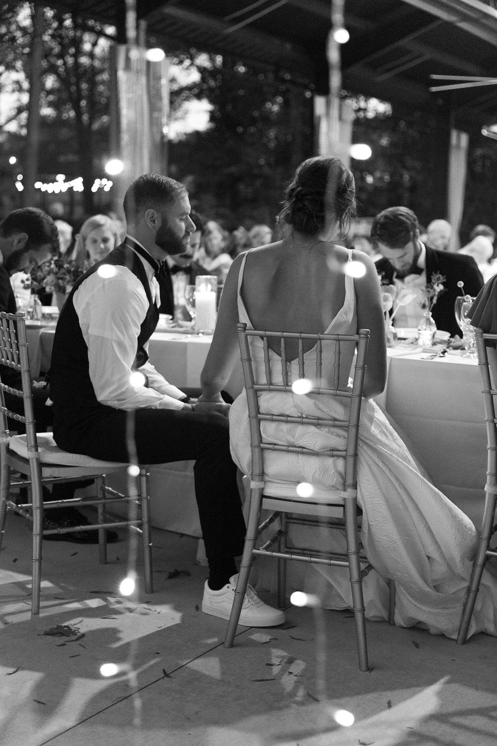 Black and white reception scene with guests seated at elegant tables under string lights.