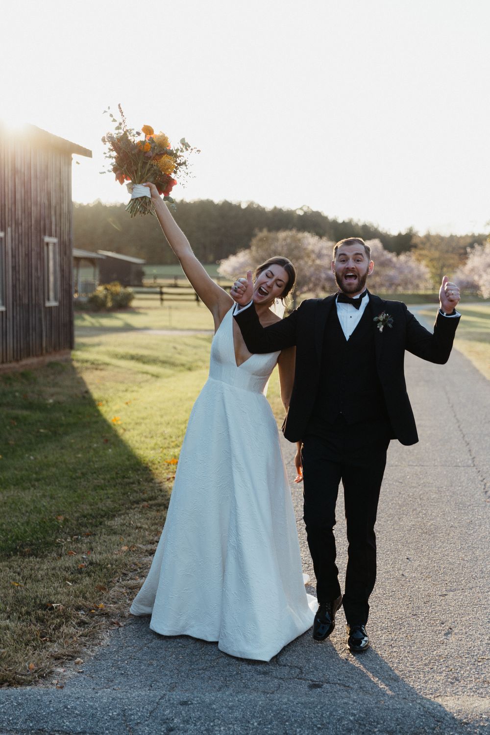 Wedding couple celebrates joyfully on a path during sunset.