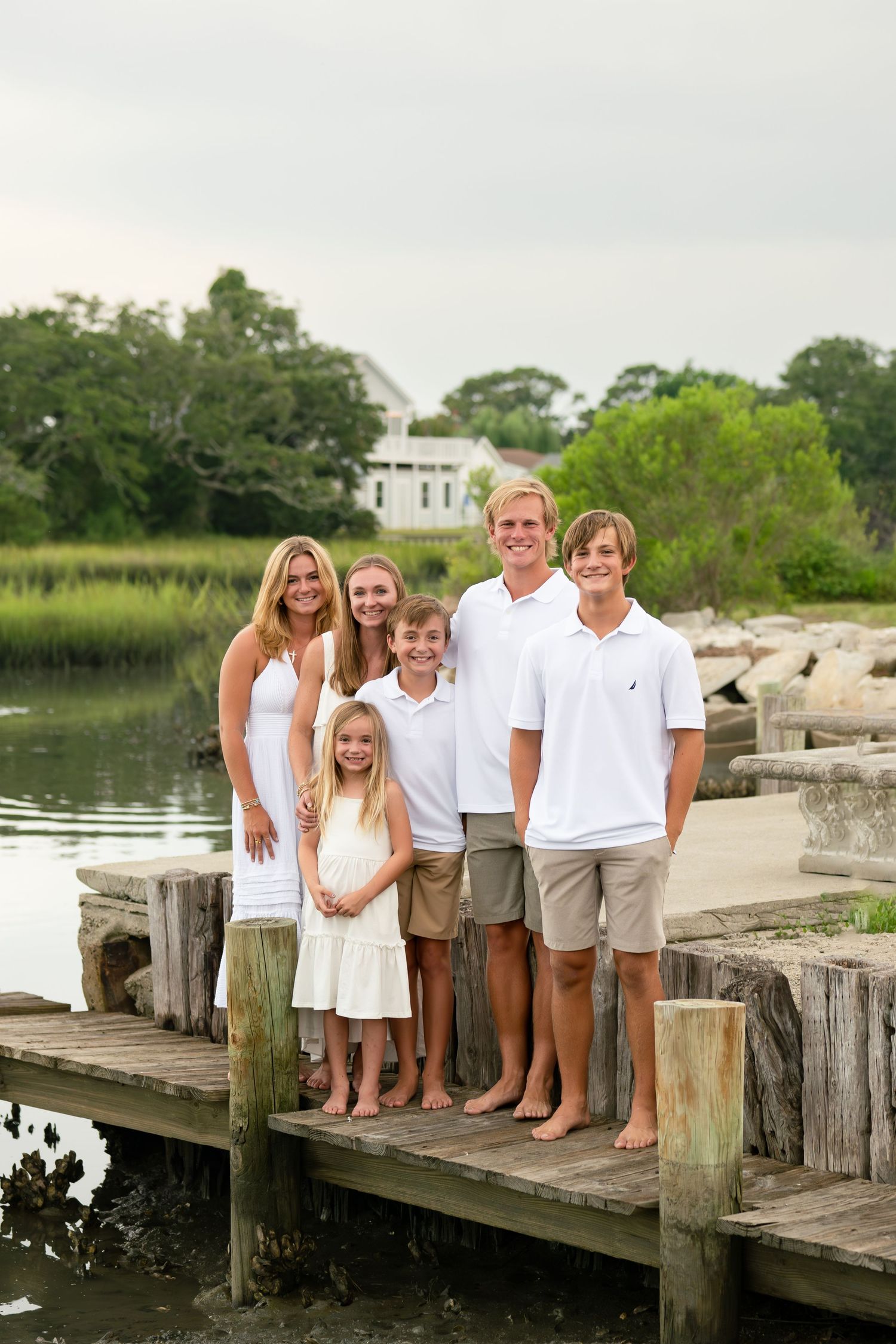 Family of four poses barefoot under a beach pier on a cloudy day.