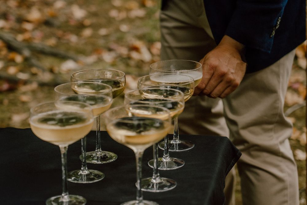 Elegant champagne coupe glasses arranged on a black table at an outdoor autumn wedding reception.