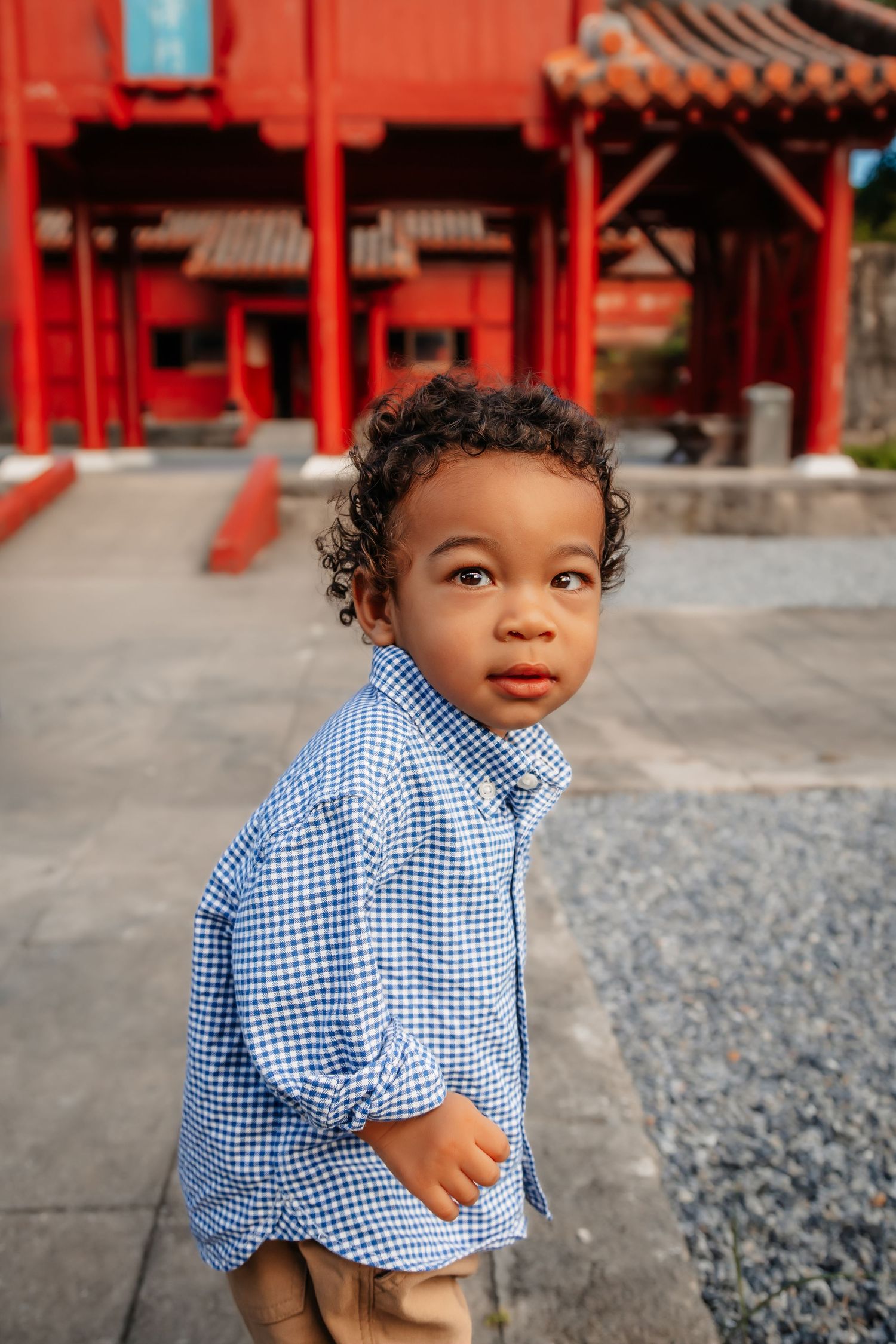 Young child in blue checkered shirt looks curiously away at traditional Asian architecture.
