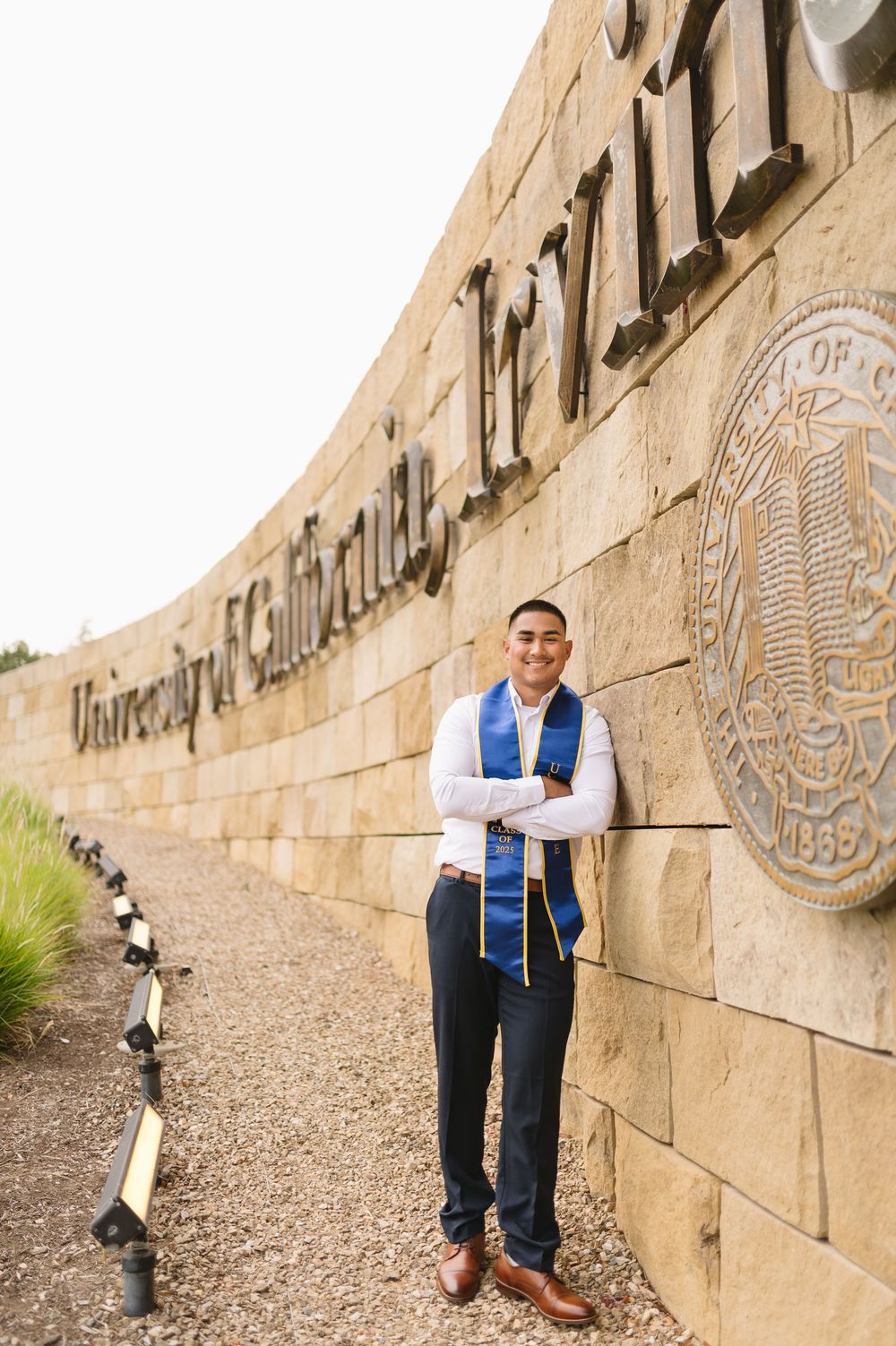 UCI graduate in cap and gown posing on the UC Irvine campus in Orange County