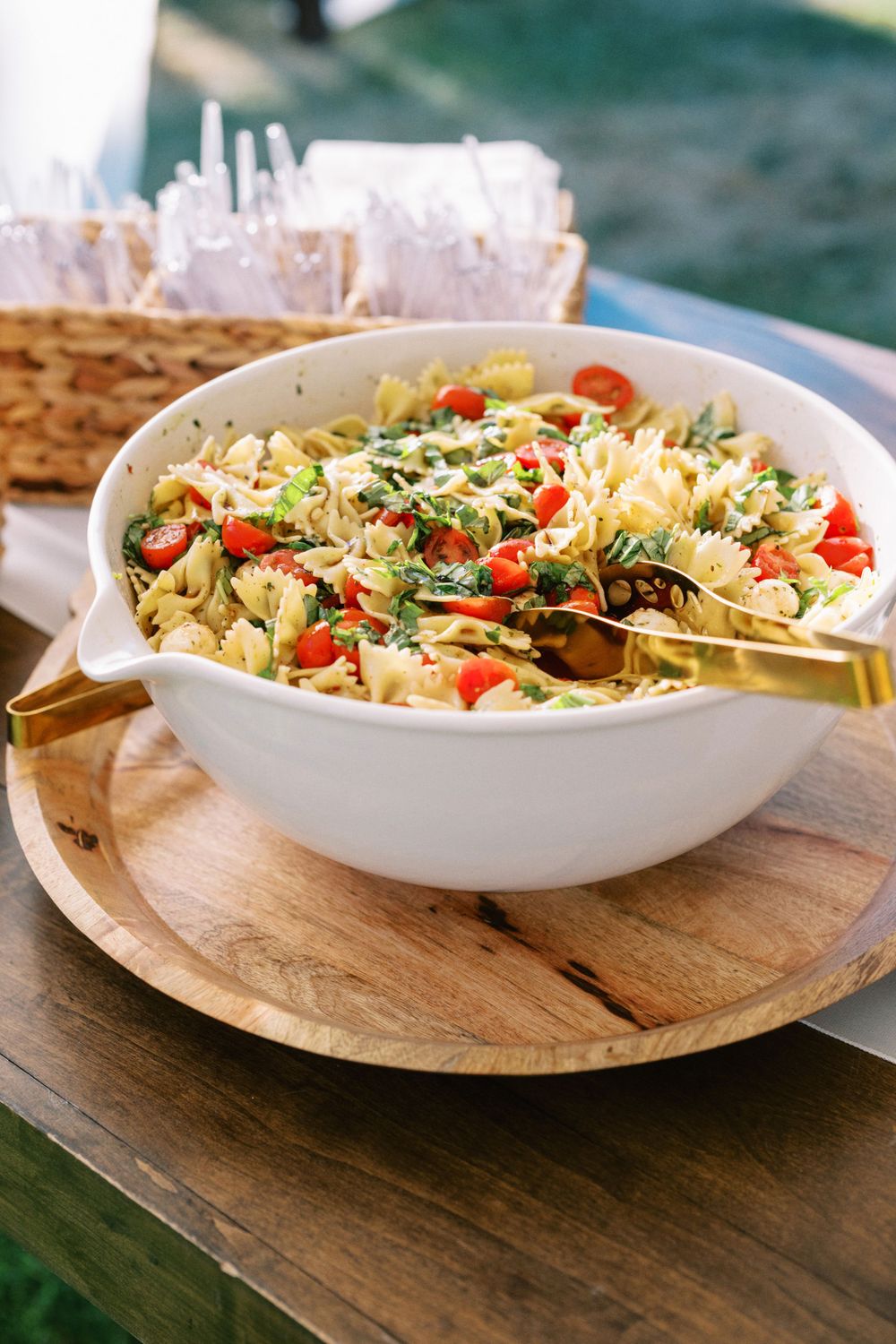 Fresh pasta salad with tomatoes and herbs served in a white bowl on a wooden serving board.