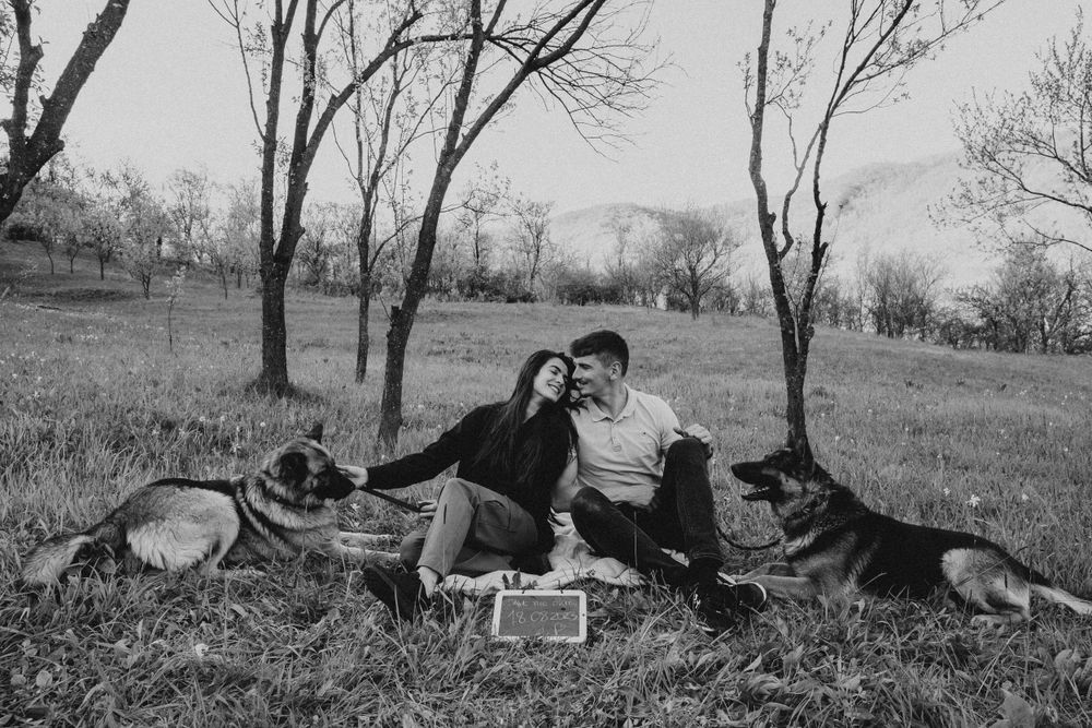 A black and white portrait of a couple with their dog in a natural outdoor setting.