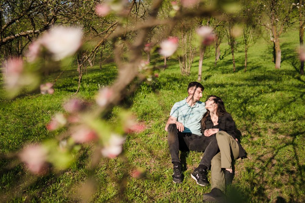Spring blossoms frame a couple and their dog relaxing in a scenic meadow setting.