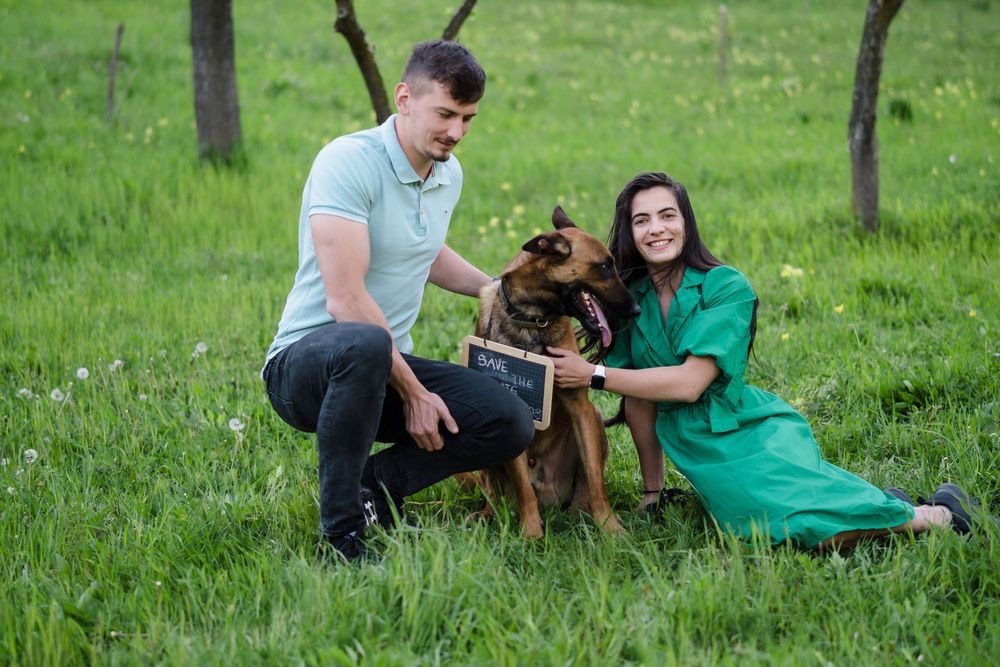 A couple relaxes on lush grass with their German Shepherd dog in a scenic park setting.