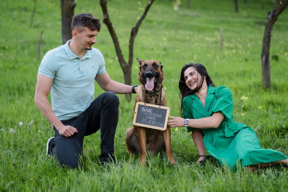 A couple and their German Shepherd dog pose together on green grass with a small chalkboard sign.