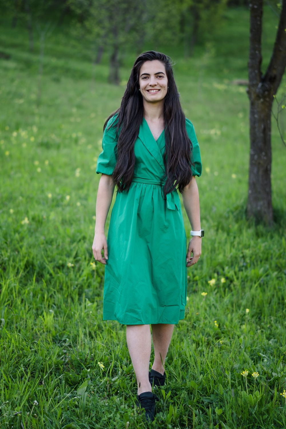 A person in an emerald green dress poses in a sunny spring meadow.