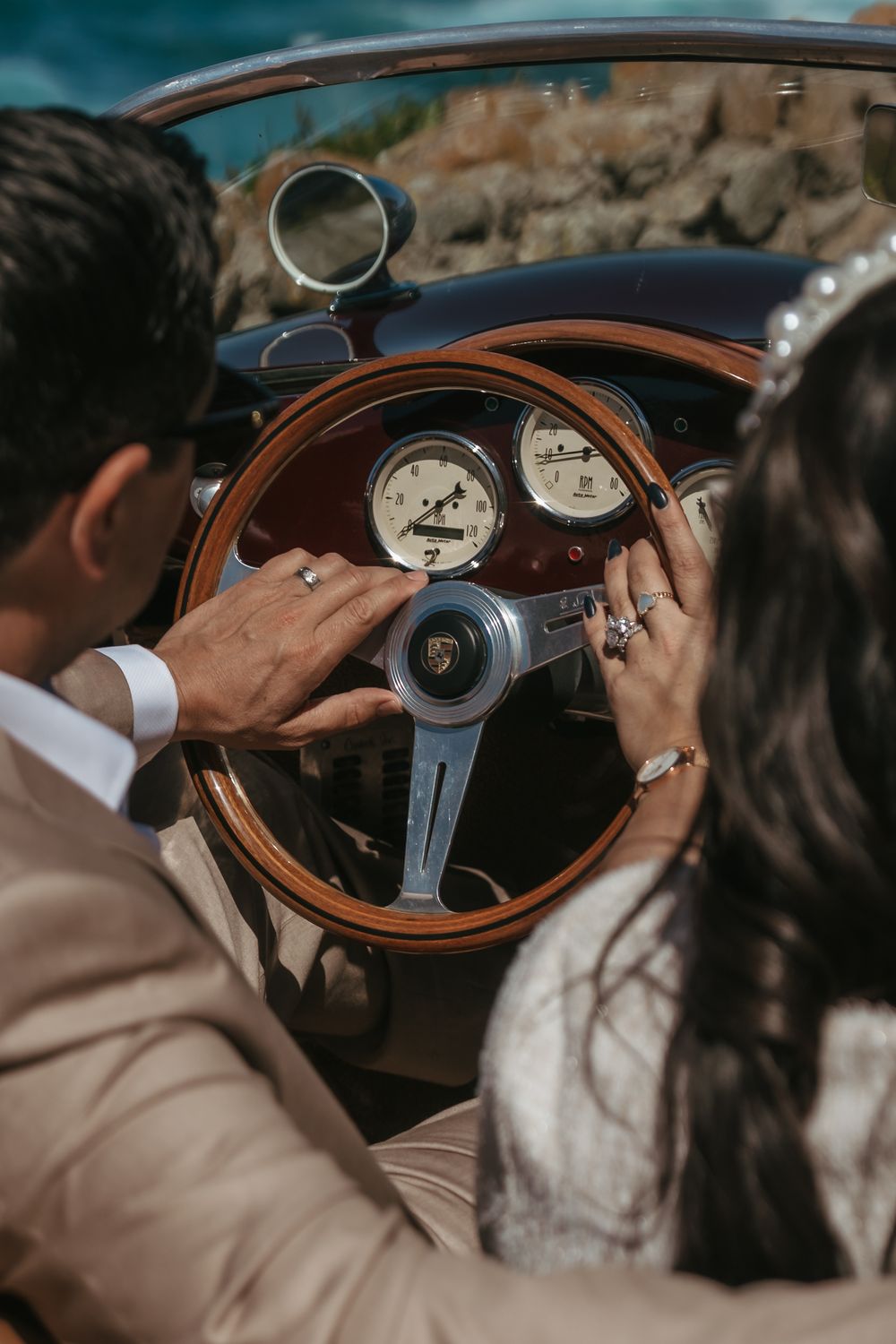Couple in wedding attire sitting in a vintage Porsche convertible with wooden steering wheel and classic gauges.