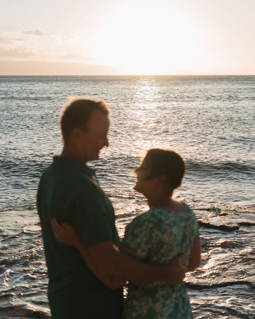 A couple embraces while silhouetted against a sunset over the ocean, creating a romantic seaside moment.