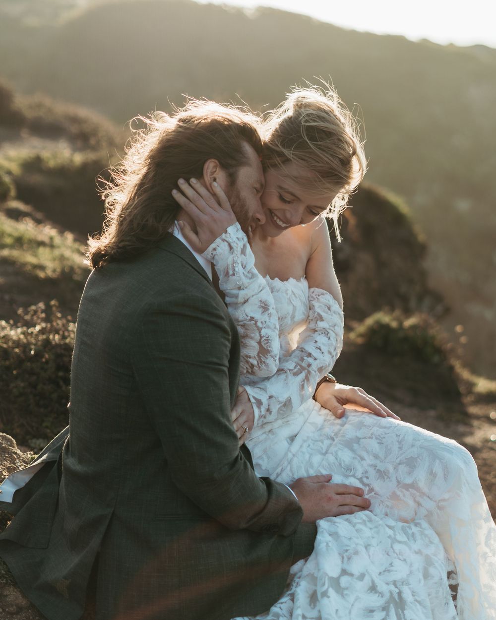 A couple embraces tenderly on a hillside at sunset, with golden light illuminating their romantic moment.