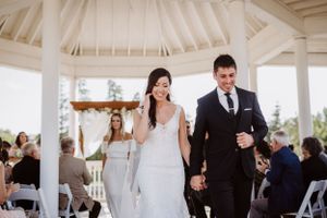 Couple walks down aisle in white gazebo after wedding ceremony while guests applaud.
