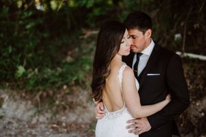 Romantic embrace between newlyweds in formal attire during outdoor wedding photoshoot.