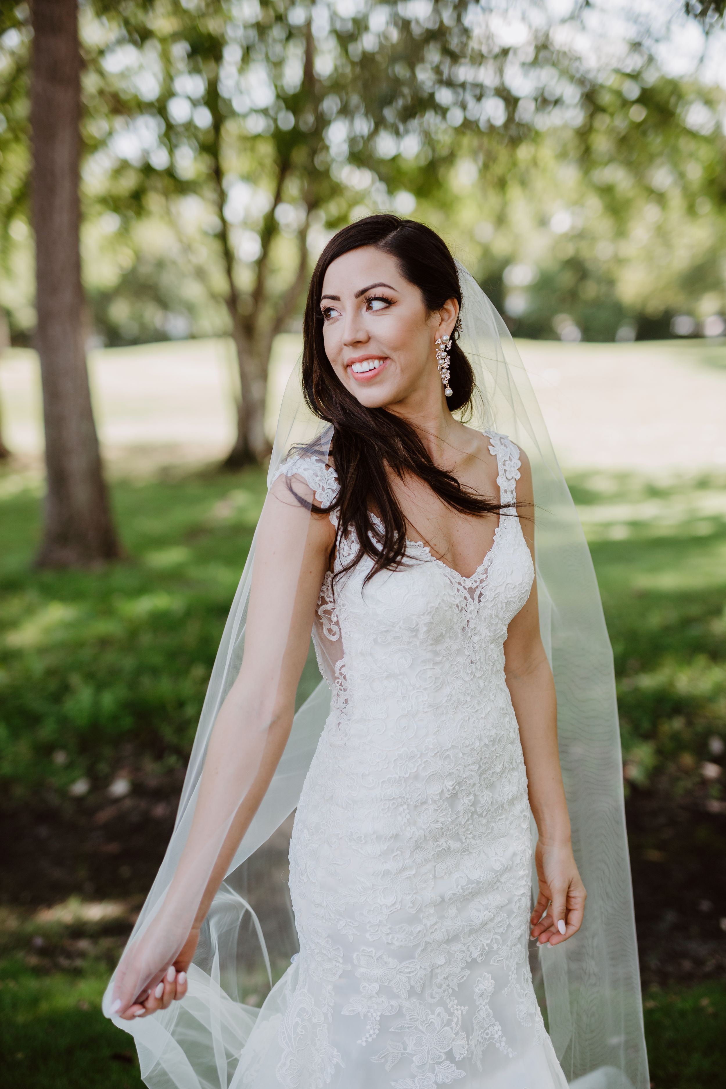 Outdoor bridal portrait featuring a lace wedding dress and flowing veil in natural lighting.