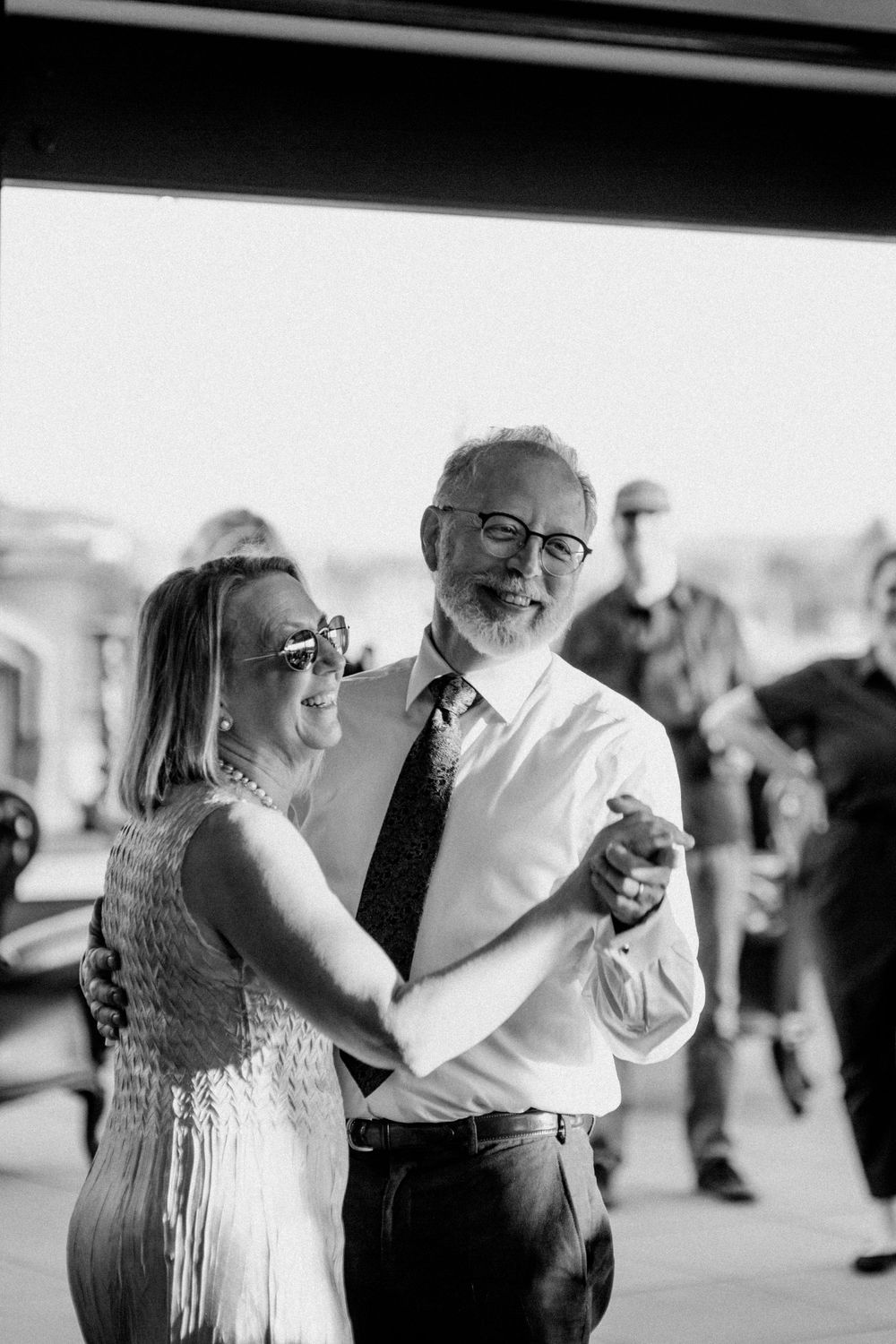 A couple shares a heartfelt dance together at an indoor venue, captured in black and white photography.