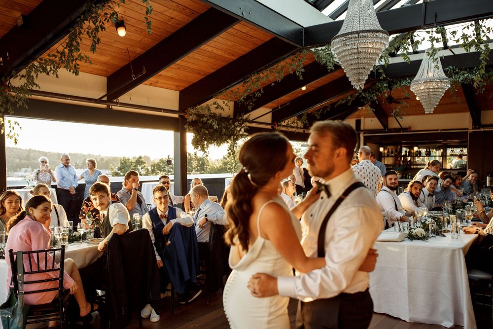 Couple shares their first dance under wooden beams and crystal chandeliers at sunset reception.