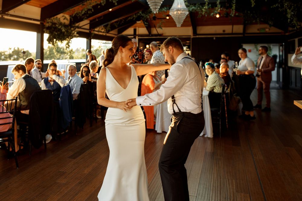 Newlyweds dancing together on wooden floor surrounded by wedding guests.