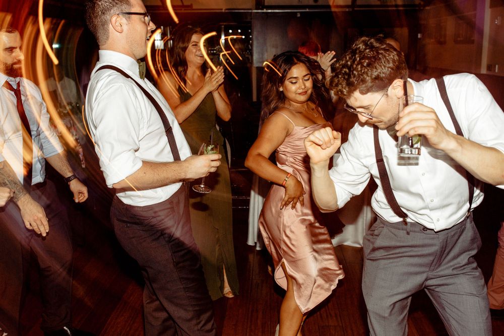 Wedding guests dancing energetically at a lively reception party with dramatic lighting.