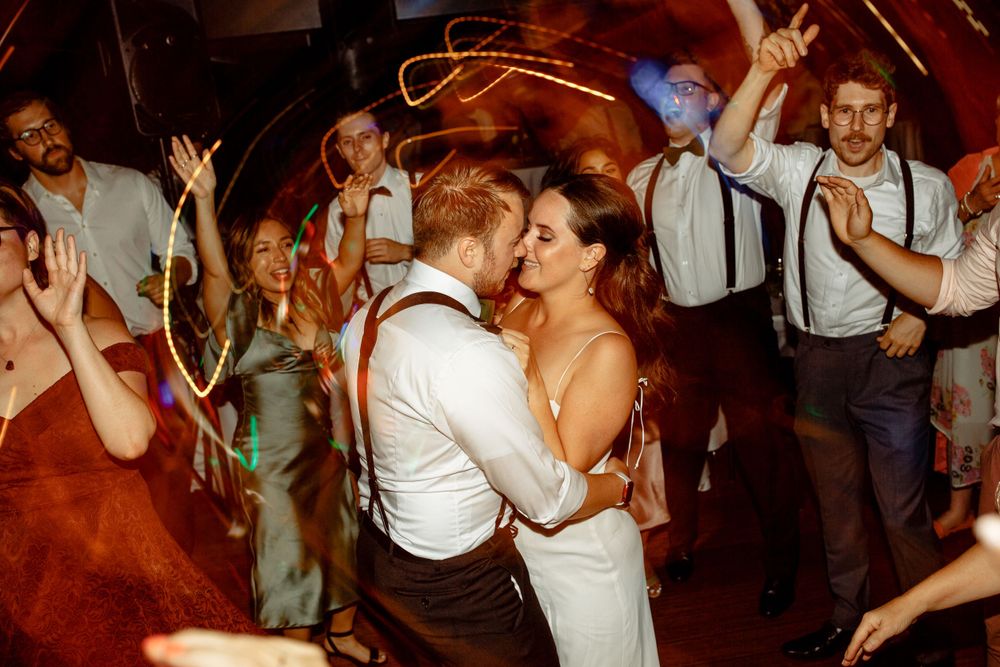 Energetic dance floor moment at wedding reception with guests in suspenders celebrating.