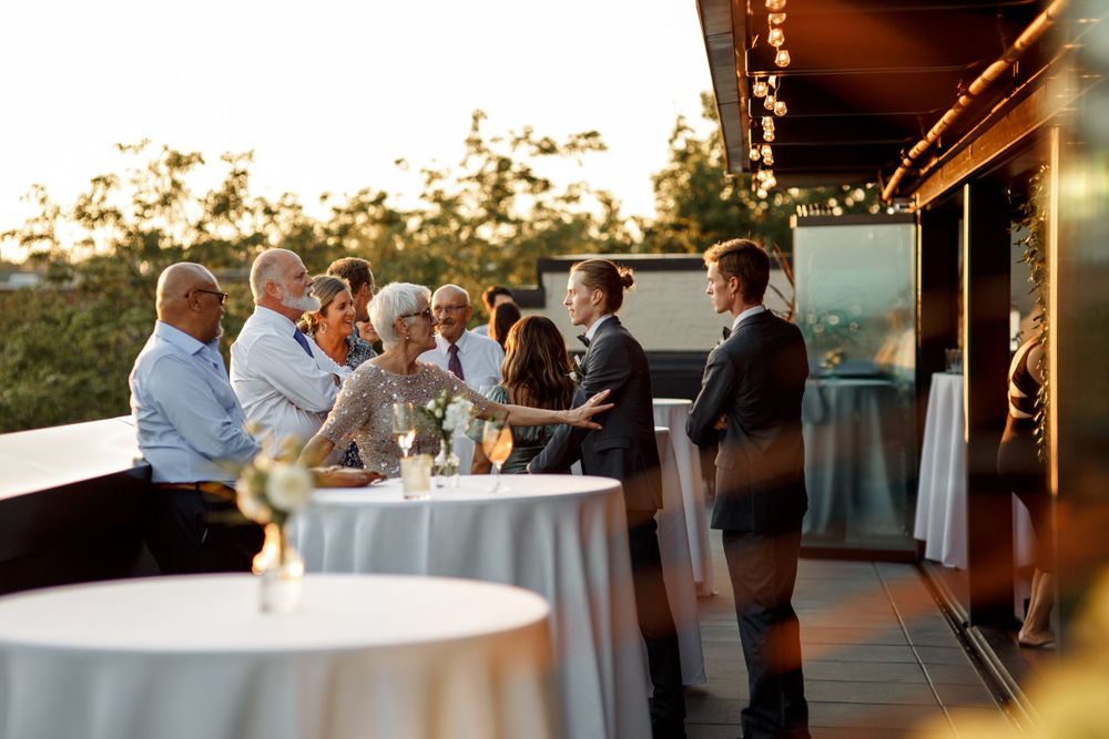 Wedding guests gather around cocktail tables on outdoor patio during sunset reception.