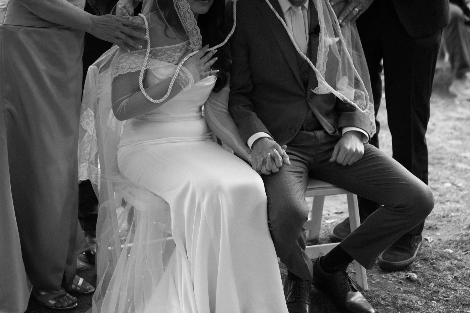 Black and white closeup photo of newlyweds sitting together at an outdoor wedding ceremony.