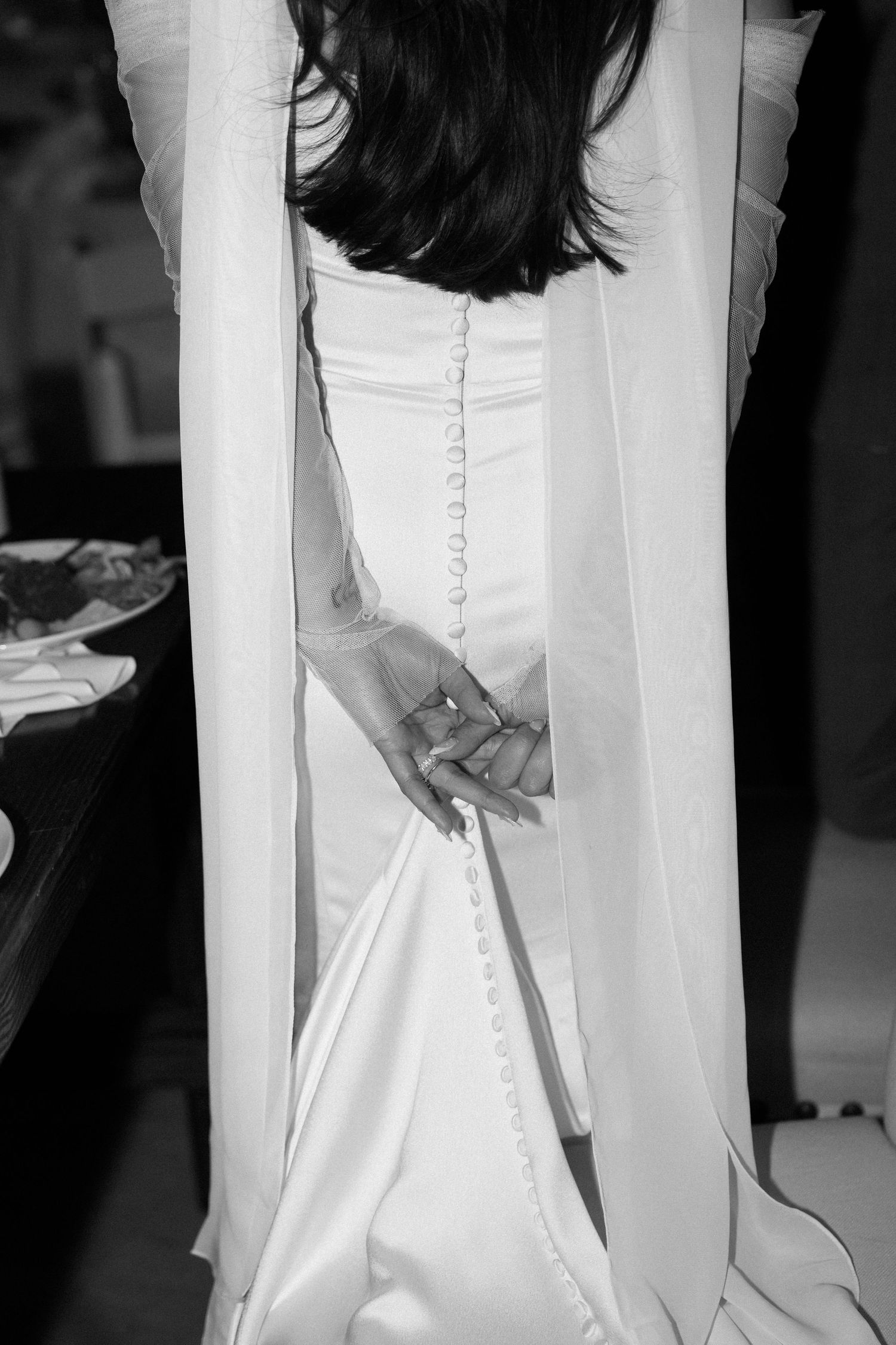 Black and white detail shot of a wedding dress showing buttons and fabric detail at the back.
