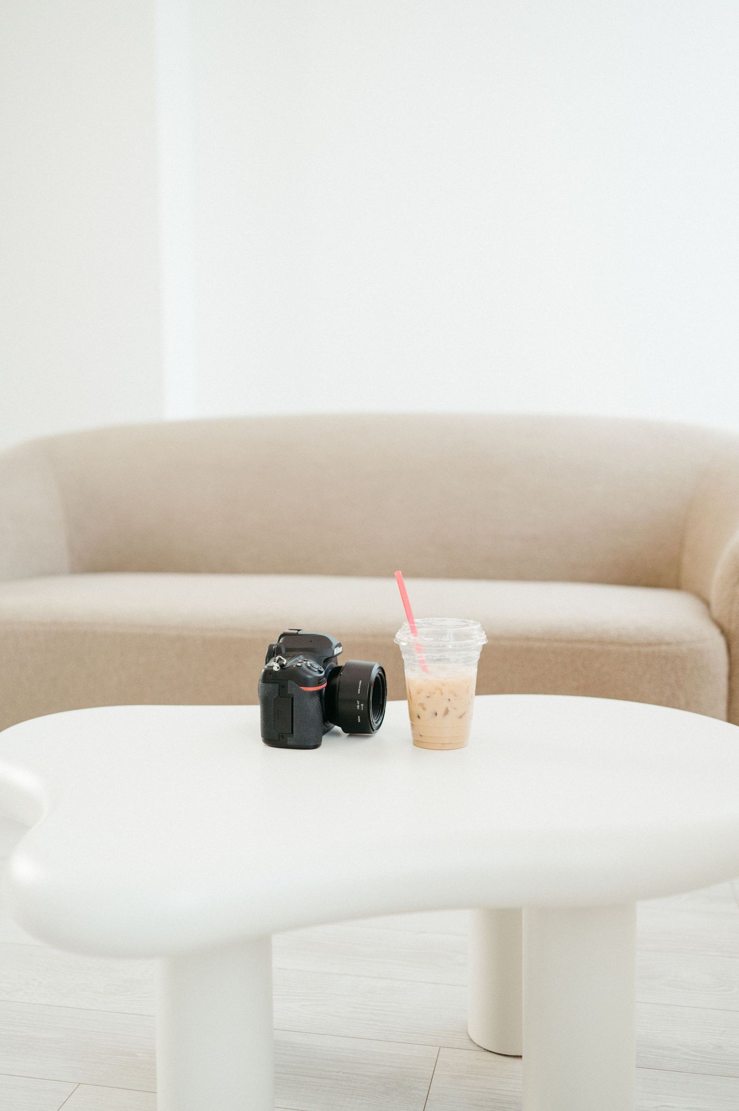 A black camera and iced coffee drink sit on a white round table with a beige couch in the background.