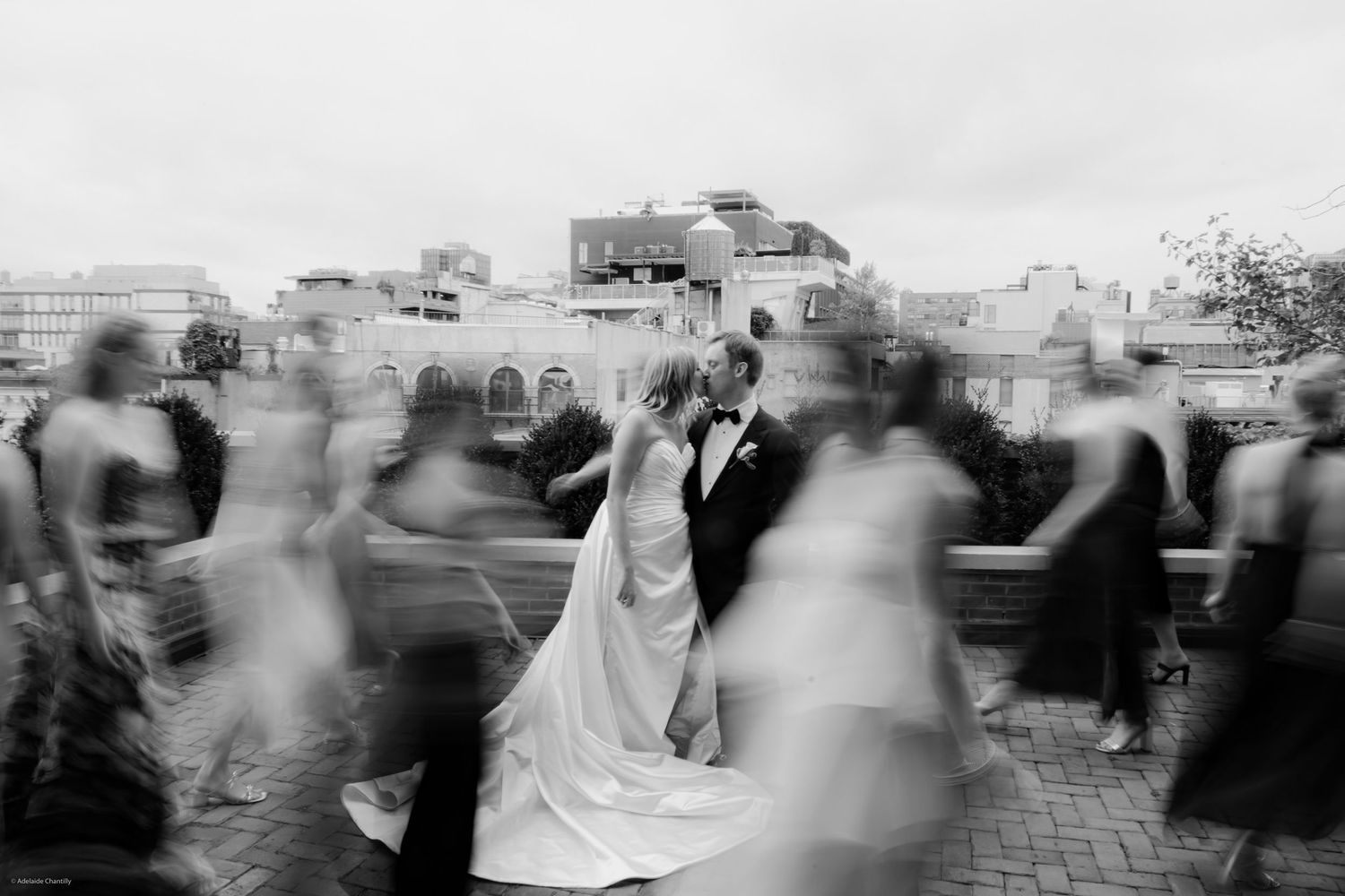 A black and white photo with a soft blur on the guests, drawing focus to the couple in the center, capturing an intimate and cinematic weddi