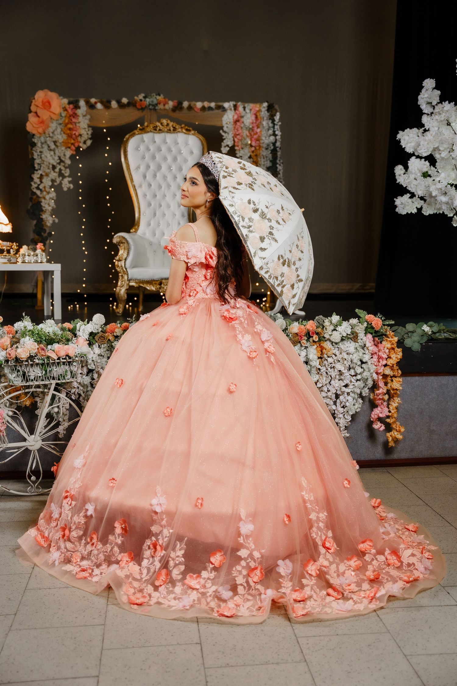 A stunning peach ballgown with floral appliques and lace details is showcased against an elegant backdrop with string lights.