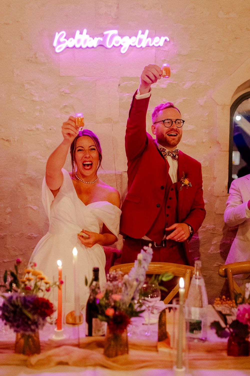 Mariés portant un toast à leurs invités pendant un mariage avec un néon "Better Together" au dessus d'eux