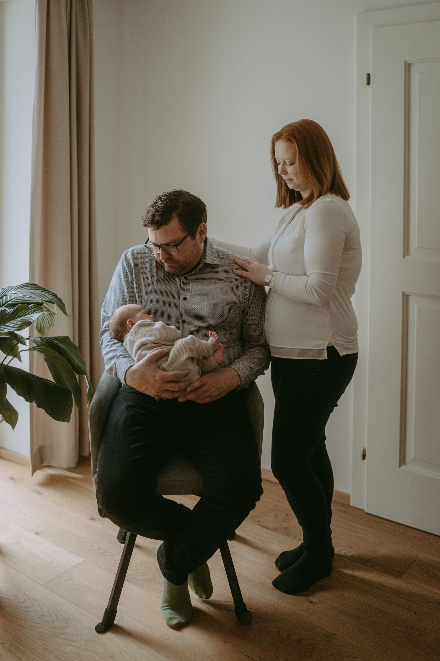 A couple shares an intimate moment with their newborn baby in a bright indoor setting.