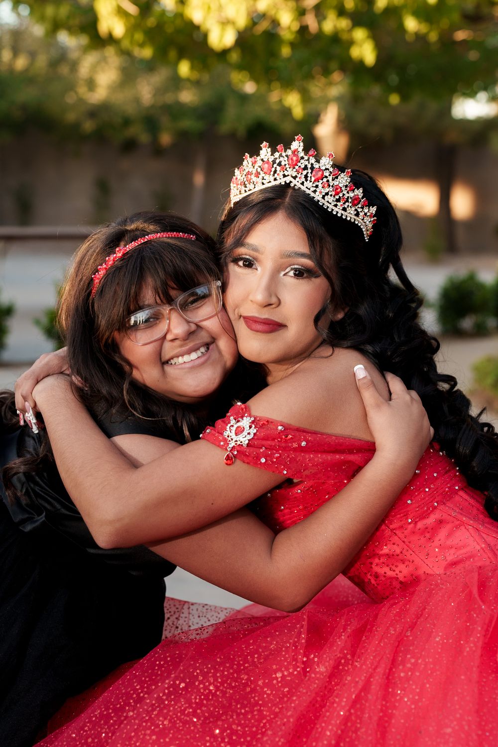 A heartwarming embrace between two figures with one wearing a sparkling red quinceañera dress and tiara.