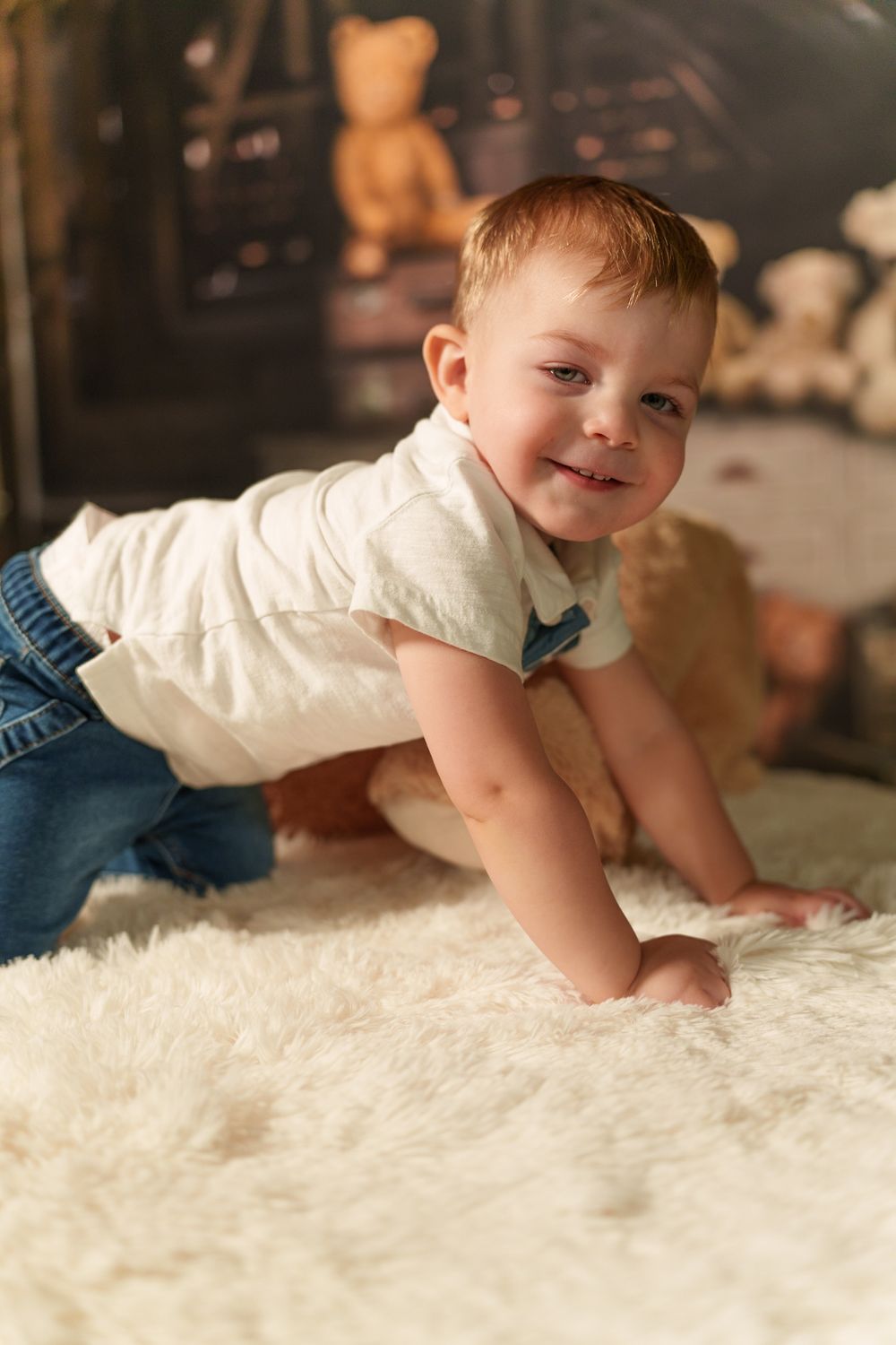 Young child crawling on plush white carpet with stuffed animals in background.