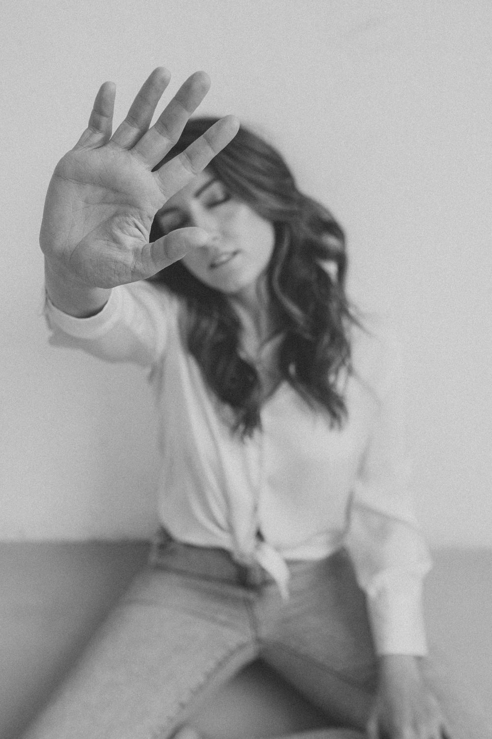 Black and white portrait of someone in casual attire holding their hand up to block the camera.