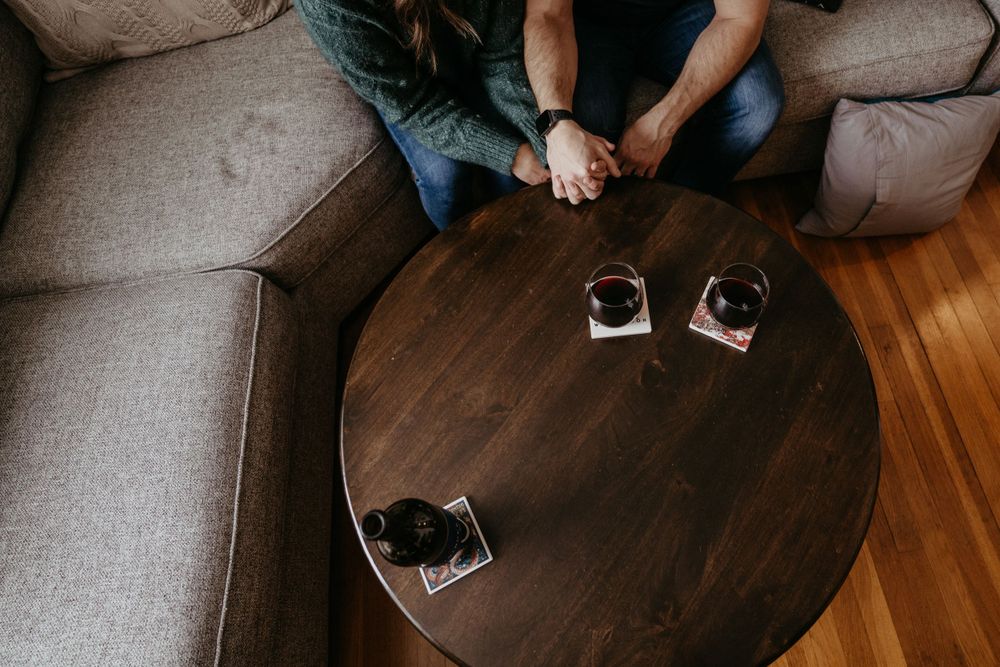 Wine glasses rest on a dark wooden coffee table in front of a gray sofa.