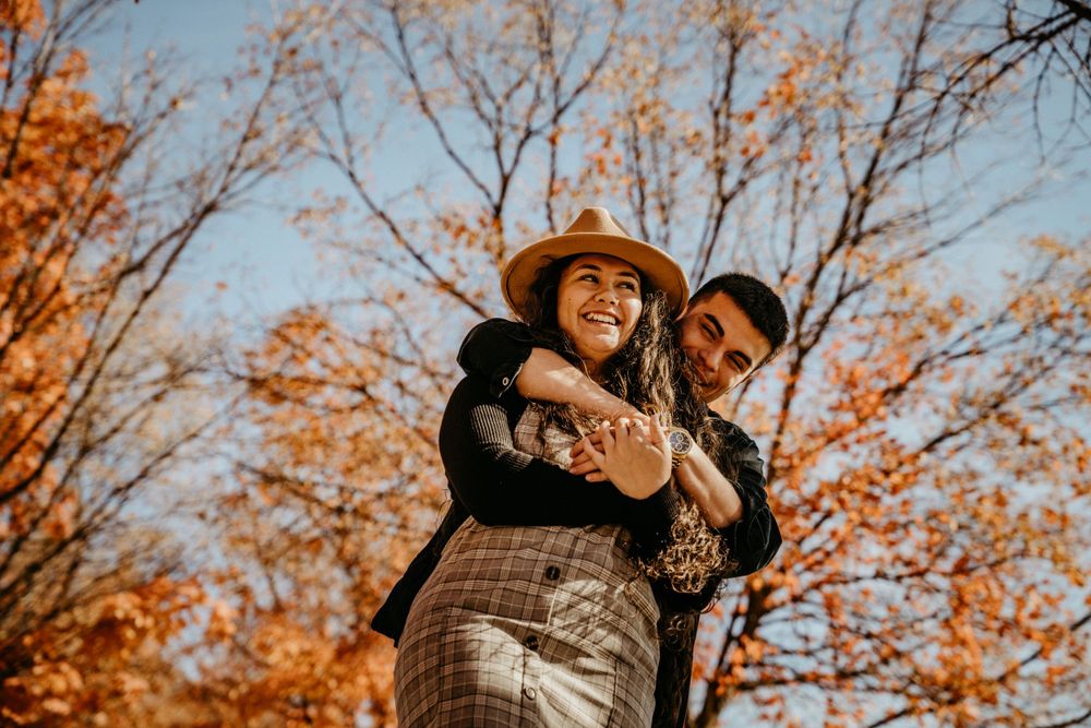 A playful embrace captured in warm sunlight with fall foliage in the background.