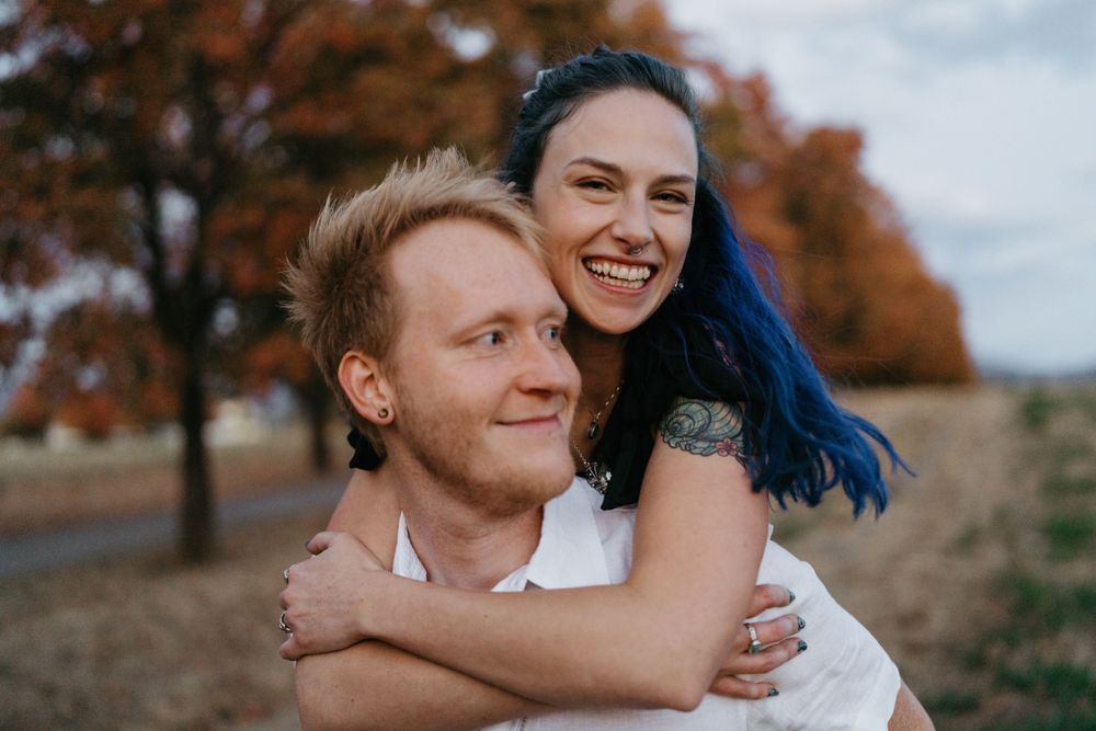 A joyful couple embraces while surrounded by fall foliage during an outdoor photo session.