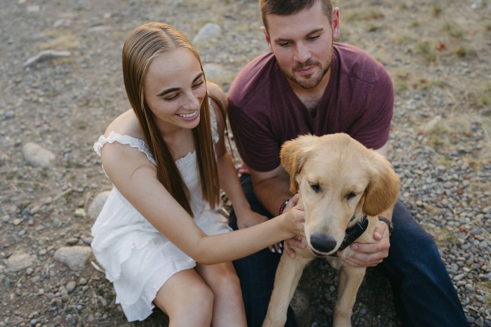 A couple sits on rocky ground with their golden retriever mix dog while petting and showing affection.