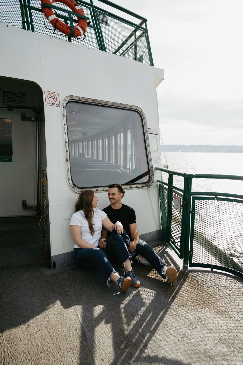 Couple sitting together on ferry boat deck, smiling and talking with ocean views in background.