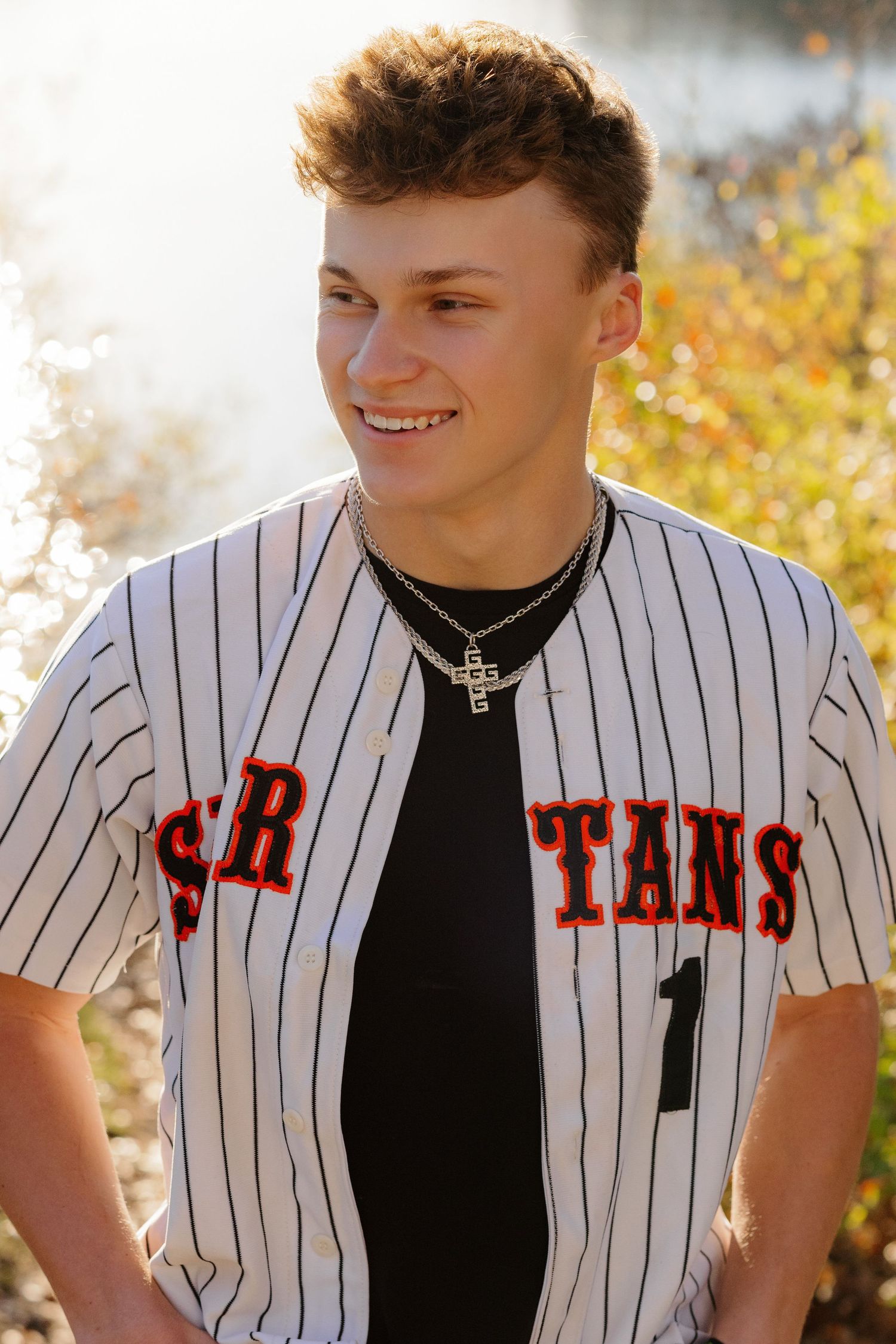 A baseball player wearing a black and white pinstriped jersey with number 1 and a cross necklace smiles outdoors.