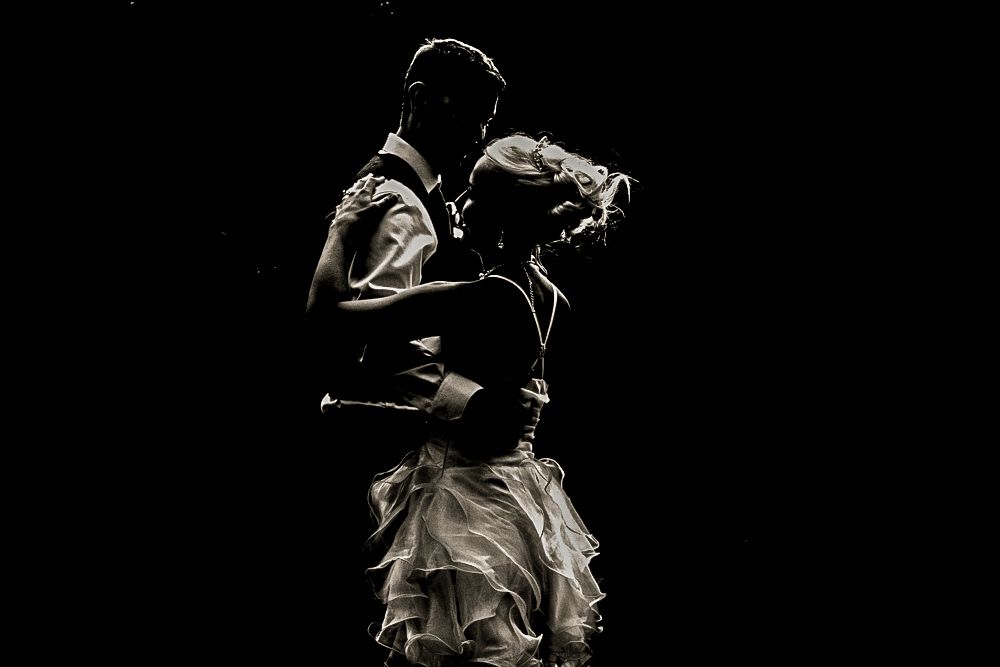 A dramatic silhouette of dancing figures in formal attire against a black background.